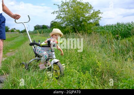 portrait of a cute little girl in a hat sitting on a small bicycle on a dirt road Stock Photo