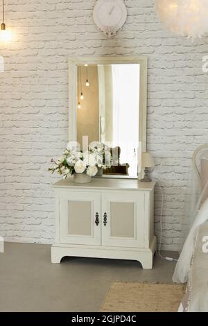 White elegant bedside table with square mirror located in bedroom as interior cosy room Stock Photo