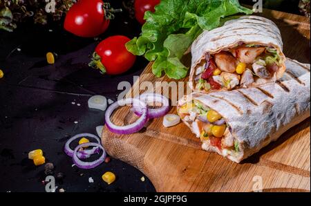 Shawarma sandwich gyro fresh roll of lavash (pita bread) with grilled meat, mushrooms, cheese, cabbage, carrots, sauce, green on dark background. Trad Stock Photo