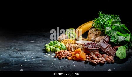 Assortment of high magnesium sources: bananas, nuts, oatmeal, buckwheat, peanuts, spinach chard, dark chocolate and sesame seeds on dark background Stock Photo