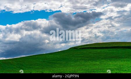 Picturesque cloudscape. Blue sky with clouds over a green field with grass. Windows desktop wallpaper example. Cloudy weather with clearings forecast. Stock Photo