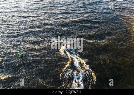 Aerial view of Young man rides on fast water scooter jumping on shallow waves and making golden splashes on sunset in blue water. Drone photo of tourist having fun riding a water bike on the sea Stock Photo