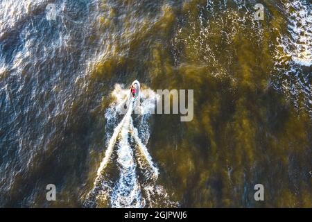 Aerial view of Young man rides on fast water scooter jumping on shallow waves and making golden splashes on sunset in blue water. Drone photo of tourist having fun riding a water bike on the sea Stock Photo