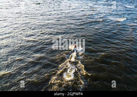 Aerial view of Young man rides on fast water scooter jumping on shallow waves and making golden splashes on sunset in blue water. Drone photo of tourist having fun riding a water bike on the sea Stock Photo