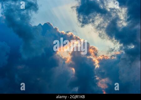 Cloudscape  with dark clouds in a warm sunset light. Rays of sun passing through stratocumulus castellanus clouds. Stock Photo