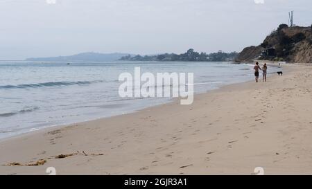 A couple walks a dog on Summerland beach in Summerland, California, USA Stock Photo