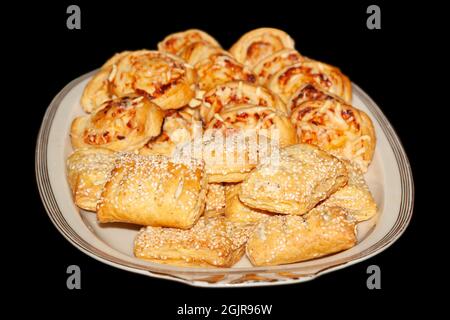 Puff pastries with cheese from the oven in a white plate, isolated on a black background Stock Photo
