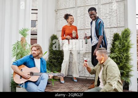 Wide angle view at diverse group of friends dancing during outdoor party at rooftop, with young man playing guitar Stock Photo