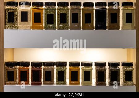 Various colorful spices in glass jars lined up on shelves Stock Photo