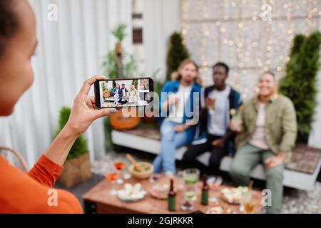 Young woman taking smartphone photo of diverse group of young people during outdoor party at rooftop Stock Photo