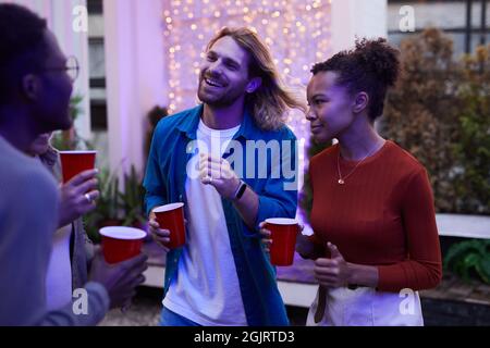 Group of carefree young people enjoying night party outdoors at rooftop lit by colored lights Stock Photo
