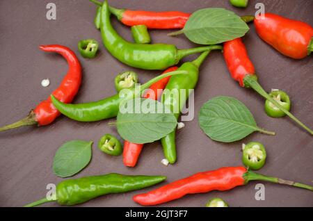 closeup the bunch red ripe sliced green chilly with green mint over out of focus brown background. Stock Photo