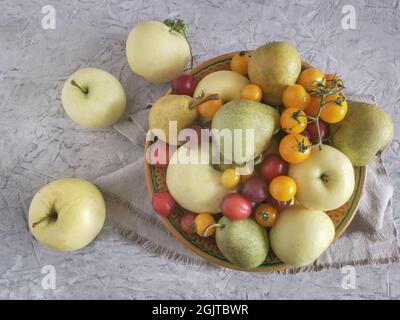 Ripe apples, pears and plums are on the table in a ceramic plate Stock Photo