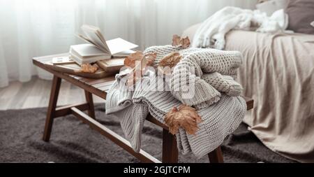 A cozy home composition with a knitted sweater, a book and leaves in the interior of the room. Stock Photo