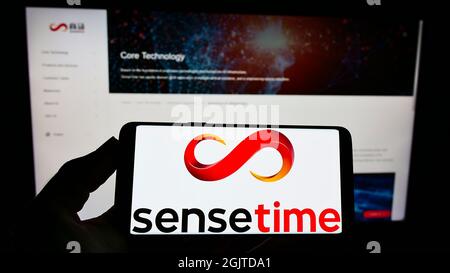 Person holding cellphone with logo of Chinese artificial intelligence company SenseTime on screen in front of webpage. Focus on phone display. Stock Photo