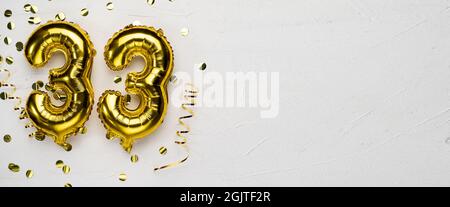 golden foil balloon number thirty three. Birthday or anniversary card with the inscription 33. gray concrete background. Anniversary celebration. Bann Stock Photo