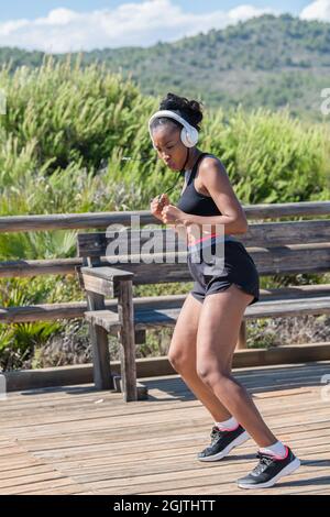 Tough afro american woman with headphones exercising outdoors: Exercise and strength concept. Stock Photo
