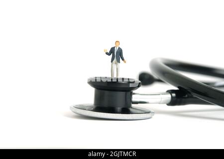 Miniature people toy figure photography. Hesitation on medical check exam concept. A shrugging businessman standing above stethoscope. Isolated on whi Stock Photo
