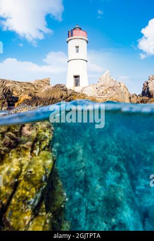 Split shot, over under shot. Half sky, half underwater. Defocused waves in the foreground with a lighthouse on a rocky coast. Stock Photo