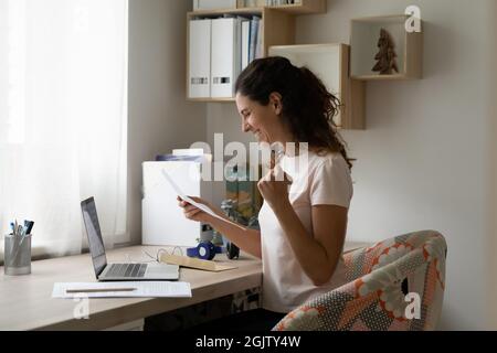 Smiling woman sitting at desk reading pleasant news in letter Stock Photo