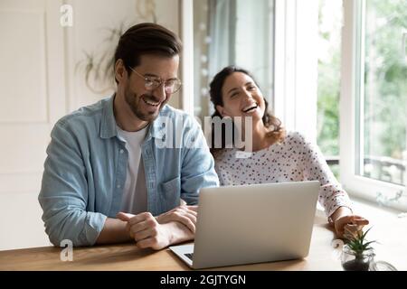 Cheerful couple laughing seated at desk in front of laptop Stock Photo