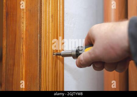 A man installs a wooden door trim. The hand screwdriver screws i Stock Photo