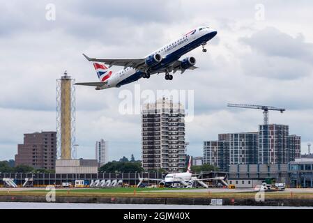 London City Airport, with a British Airways, BA Cityflyer Embraer ERJ 190 airliner jet plane taking off, with residential tower block housing. Flight Stock Photo