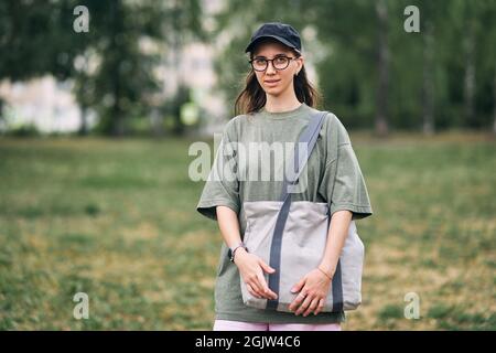 Young woman with glasses holding empty cotton eco bag, mockup design. Stock Photo