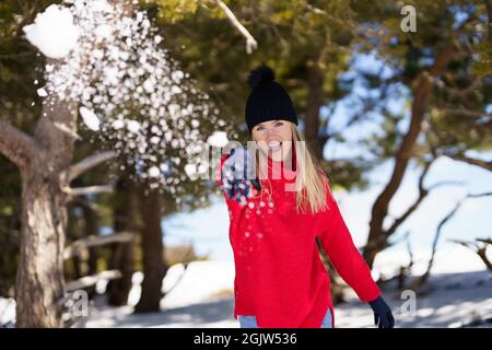 Young woman throwing snowballs forward in a snow-covered forest in the mountains Stock Photo