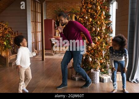 Happy biracial father and kids dance near fir tree Stock Photo