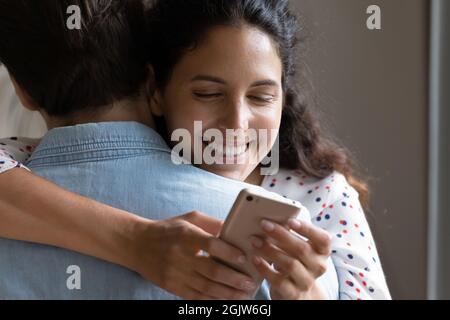 Smiling woman holding cellphone using e-date application while hugging husband Stock Photo