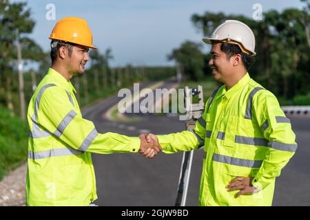 Asian survey engineers handshake on road construction site, after use theodolite mark a expressway at highway success, Civil Engineers, Surveyor equip Stock Photo