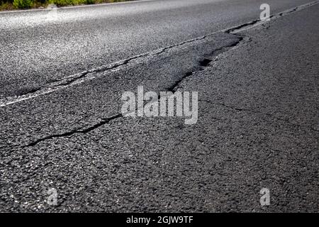 Close up of asphalt road surface crack with rural landscape in a background. Stock Photo