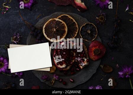 Ripe pomegranate in a vintage plate, a bunch of dry grapes and orange slices with business cards Stock Photo