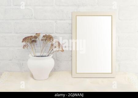 Empty white frame mockup with a bouquet of dry flowers in a vintage vase on a linen fabric  in Provence style against a background of a white brick wa Stock Photo