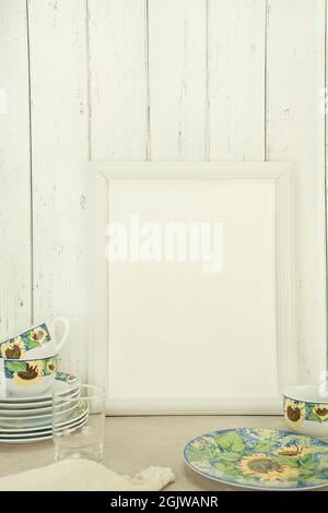 Empty white frame mockup with dishes on table against white wall background Stock Photo