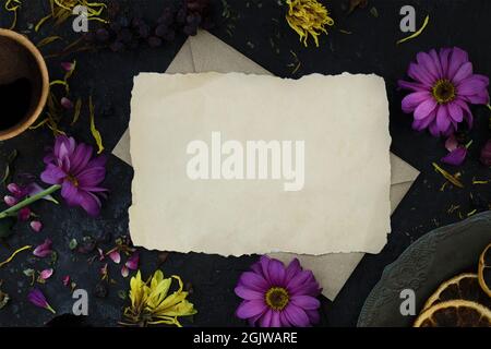 Mockup of letter on an envelope among wilted flowers, a cup of coffee and a vintage plate. Top view. Melancholic mood Stock Photo