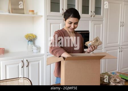 Satisfied young indian woman unpack box with groceries ordered online Stock Photo