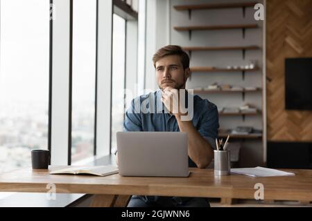 Pensive male employee work on laptop thinking Stock Photo