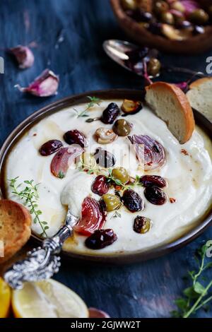 Greek feta cheese dip, Tirokafteri, with roasted olives, garlic, red onions, drizzled with olive oil and garnished with thyme. Selective focus on cent Stock Photo