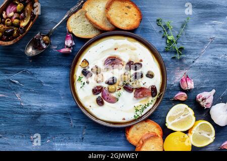 Flatlay of Greek feta cheese dip, Tirokafteri, with roasted olives, Italian garlic, red onions or shallots, drizzled with olive oil and garnished with Stock Photo