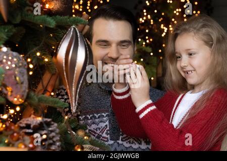 Happy young father decorating christmas tree with small daughter. Stock Photo