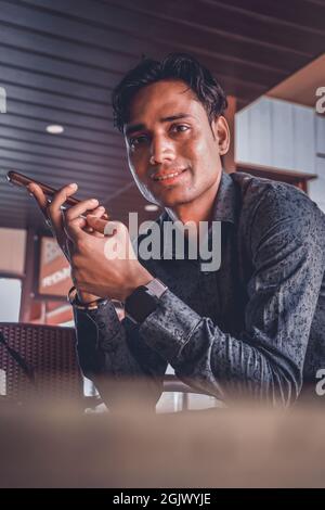 A handsome smiling Indian male in a shirt using a smartphone Stock Photo