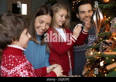 Happy loving family involved in decorating x-mas festive evergreen tree. Stock Photo