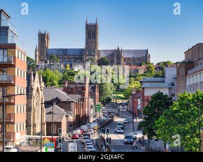 2 July 2019:Lincoln, UK - A view of the cathedral, along Broadgate, a busy city centre street full of traffic., with clear blue sky and trees in full Stock Photo