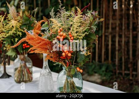 Rustic style. Boho style bouquets on the table in glass vases and jars. Wooden table and white tablecloth Stock Photo