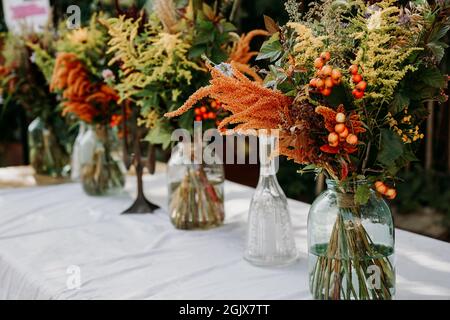Rustic style. Boho style bouquets on the table in glass vases and jars. Wooden table and white tablecloth Stock Photo