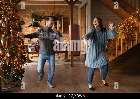Overjoyed crazy young married family couple dancing near Christmas tree.