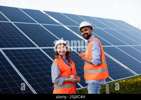 Two engineers in uniform are standing at the background of solar panels and discuss the situation Stock Photo