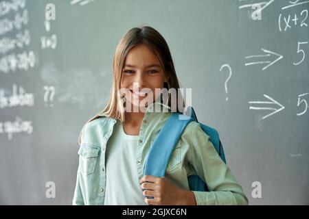Portrait of happy smiling hispanic girl standing on chalkboard background. Stock Photo